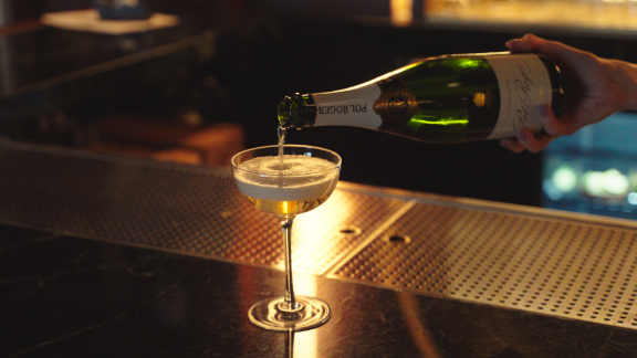Bartender pouring champagne into a coupe glass at Metro Private Cinema’s cocktail bar