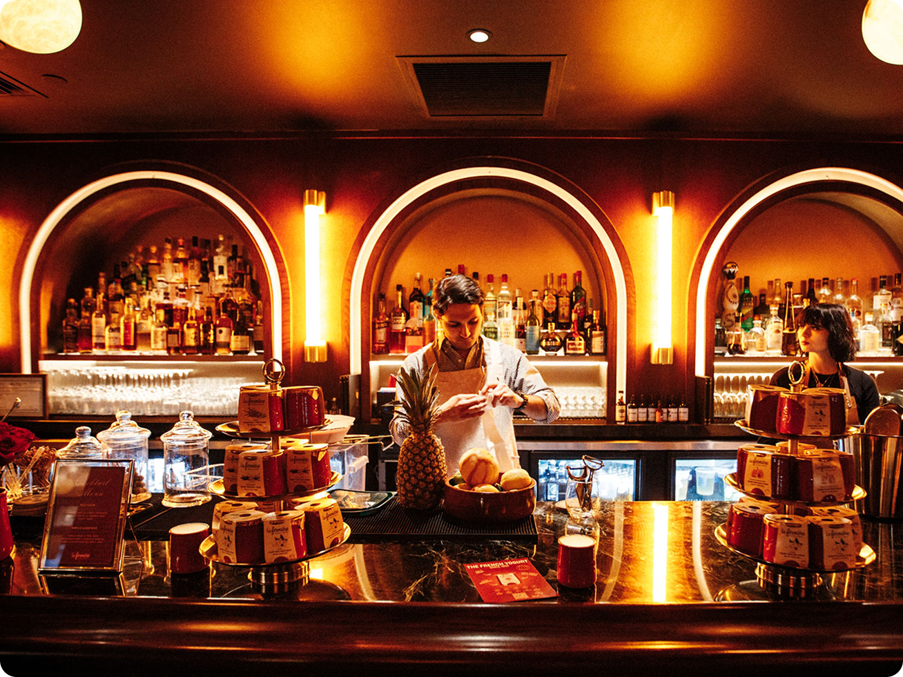 A bartender preparing drinks behind a warmly lit, arched bar at Metro.
