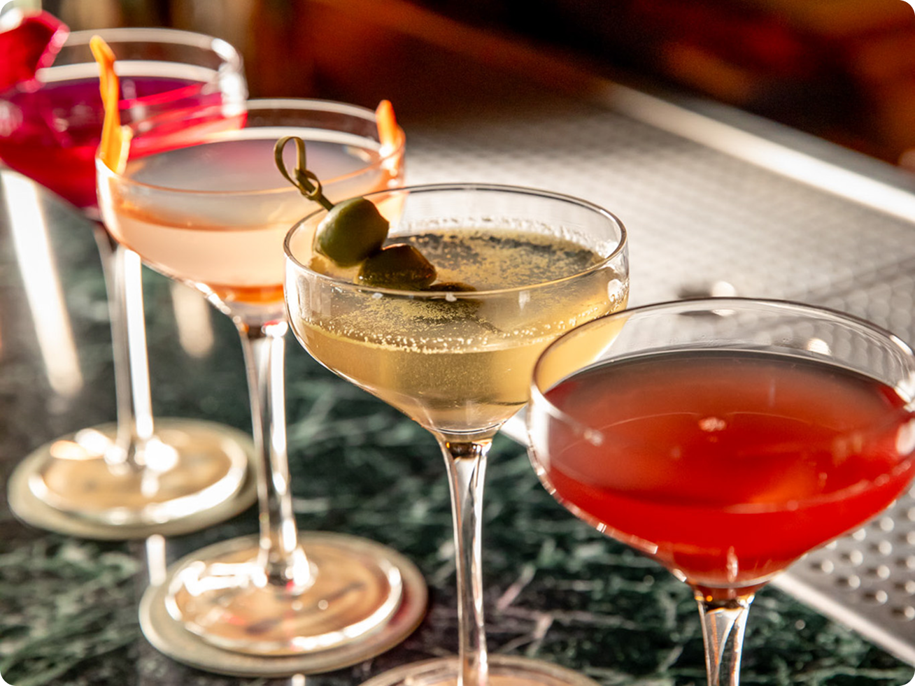 A row of colorful martinis and cocktails in coupe glasses.
