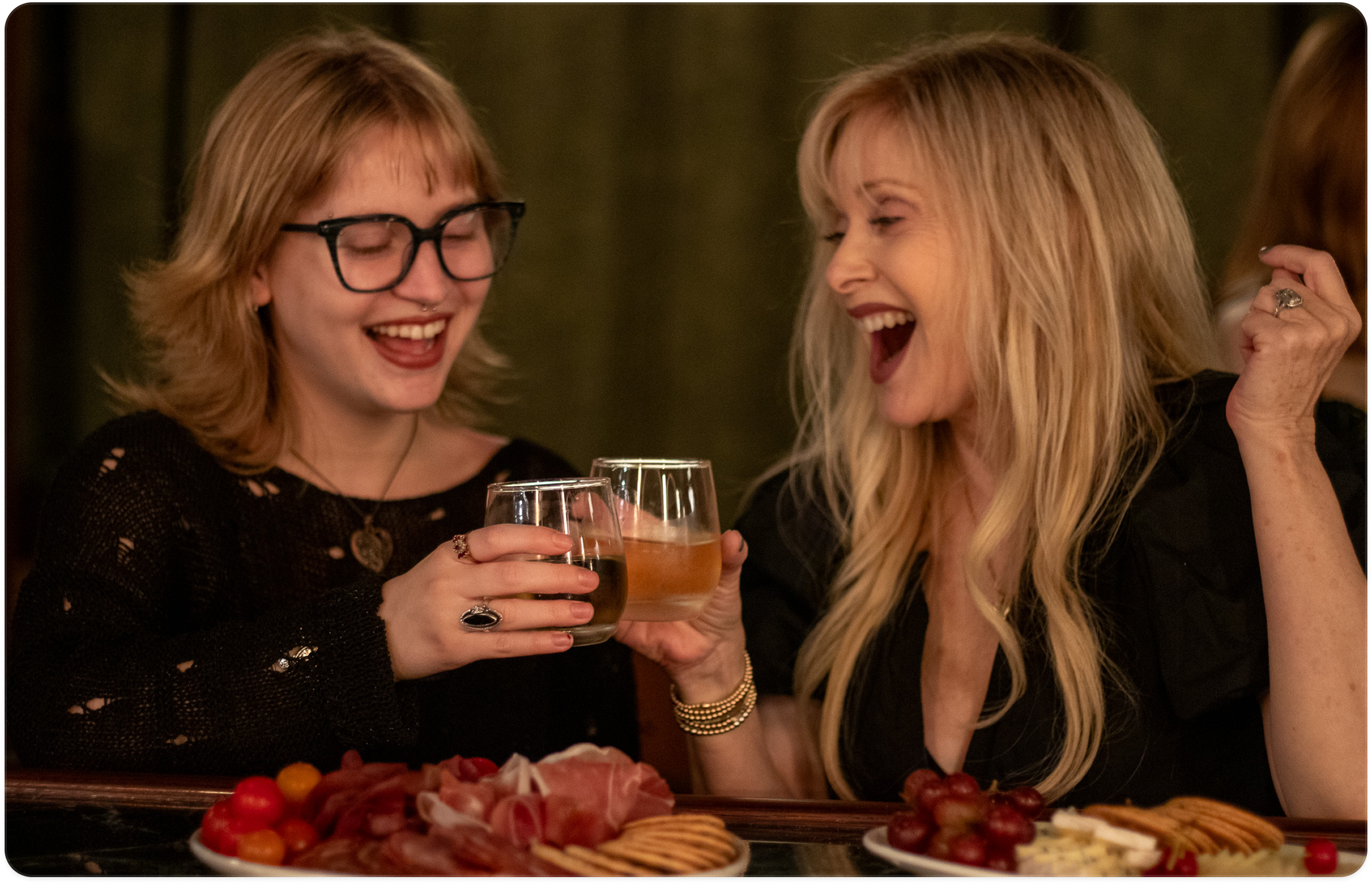 Two women laughing and clinking glasses at the bar.